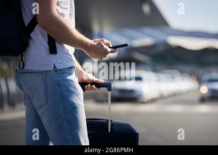 Uomo che tiene lo smartphone e utilizza l'app mobile contro una fila di taxi. Temi tecnologia moderna, carsharing e viaggi. Foto Stock