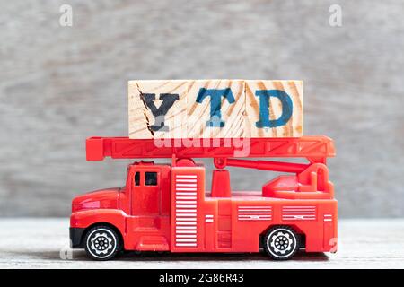 Il camion fuoco rosso tiene il blocco di lettera in parola YTD (abbreviazione di anno ad oggi) su sfondo di legno Foto Stock