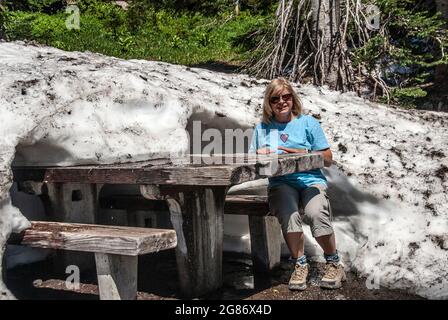 Giovane donna seduto al tavolo da picnic sepolto nella deriva della neve, Mt. Rainer National Park, Washington Foto Stock