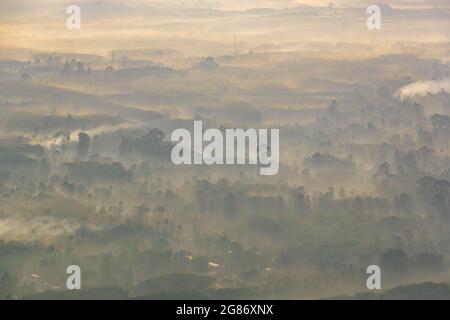 Alba con raggi solari illuminato la bella vista del piccolo villaggio circondato da nebbia morbida. Ampio angolo paesaggio di strati di montagna al mattino Foto Stock