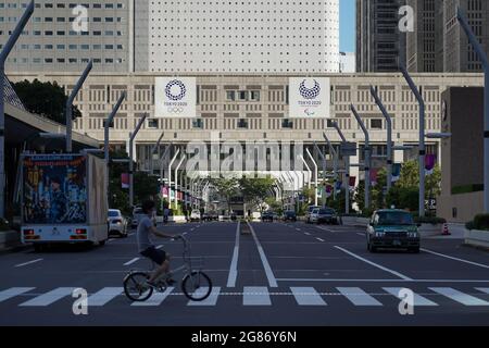 Shinjuku, Giappone. 17 luglio 2021. Un uomo in bicicletta attraversa una strada vicino all'edificio del governo metropolitano di Tokyo, dove sono esposti i banner dei Giochi Olimpici e Paralimpici di Tokyo 2020. I Giochi Olimpici di Tokyo 2020, ufficialmente noti come Giochi della XXXII Olympias, si terranno dal 23 luglio all'8 agosto 2021 a Tokyo Credit: SOPA Images Limited/Alamy Live News Foto Stock