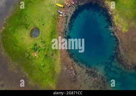 Viev aereo di imbarcazioni tradizionali parcheggiate dall'occhio di Shegan (Syri i Sheganit) sorgente di colore blu intenso, Lago Shkodra, preso dal drone, Albania Foto Stock