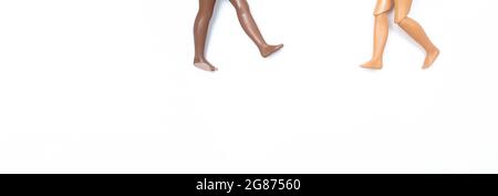 Due paia di gambe di bambole giocattolo che vanno l'una all'altra su sfondo bianco. Diverse tonalità della pelle e razze. Fermare il razzismo. Concetto di diversità e unità Foto Stock