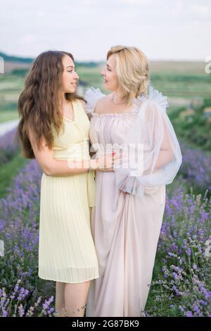 Madre e figlia nel campo di lavanda in bella giornata estiva. Splendida signora bionda di mezza età in piedi al campo di lavanda con la sua bella figlia giovane e godendo la passeggiata Foto Stock