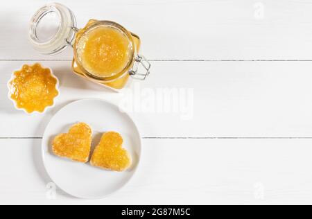 Marmellata di frutta fresca su sfondo bianco di legno. Brindate i cuori in un piatto. Confiture gialle. Spazio per il testo. Vista dall'alto, disposizione piatta. Foto Stock