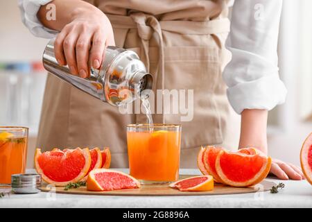 Donna che versa il succo di pompelmo in un bicchiere sul tavolo luminoso in cucina Foto Stock