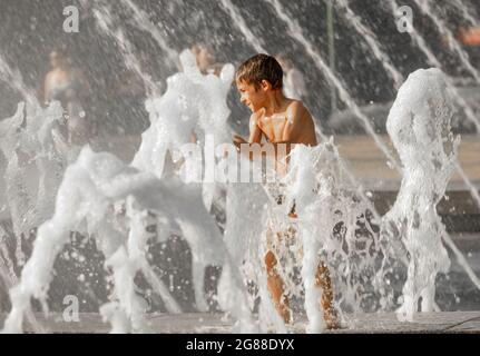 Ragazzo che gioca con i getti di acqua frothy fontana, in estate durante l'onda di calore Foto Stock