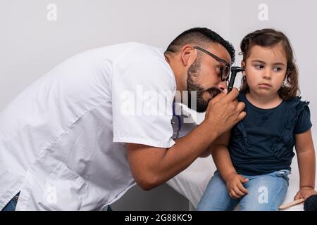 Pediatra caucasica trentenne che esamina le orecchie del suo paziente, una bambina caucasica di tre anni. Concetto pediatrico. Foto Stock