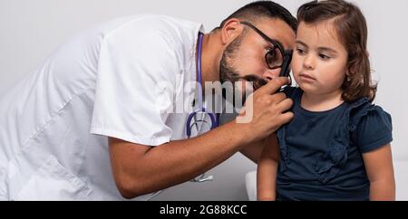 Pediatra caucasica trentenne che esamina le orecchie del suo paziente, una bambina caucasica di tre anni. Concetto pediatrico. Foto Stock