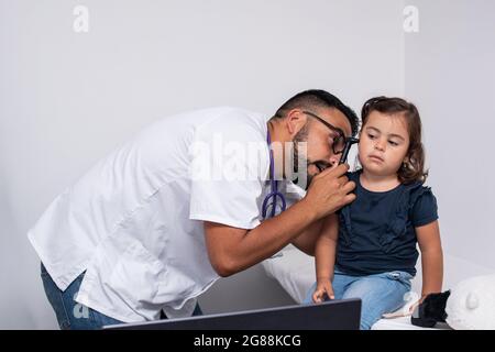 Pediatra caucasica trentenne che esamina le orecchie del suo paziente, una bambina caucasica di tre anni. Concetto pediatrico. Foto Stock