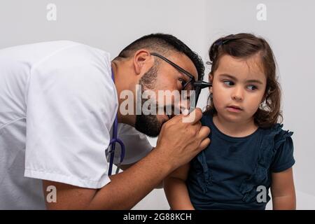 Pediatra caucasica trentenne che esamina le orecchie del suo paziente, una bambina caucasica di tre anni. Concetto pediatrico. Foto Stock