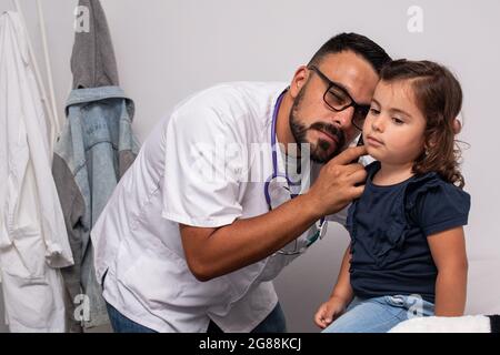 Pediatra caucasica trentenne che esamina le orecchie del suo paziente, una bambina caucasica di tre anni. Concetto pediatrico. Foto Stock