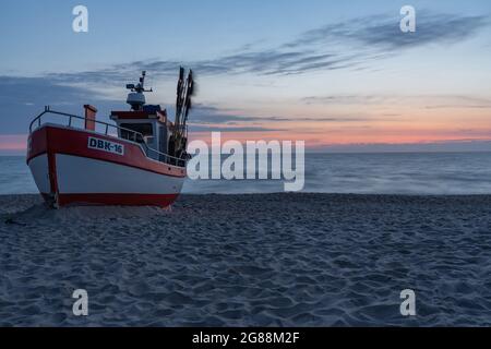 Barca da pesca su una spiaggia di sabbia al tramonto con uno sfondo di mare sfocato Foto Stock