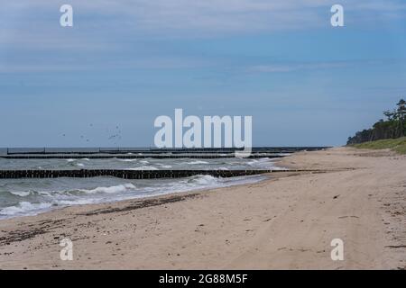 Onde di mare che si infrangono contro una frangiflutti di legno direttamente sulla spiaggia Foto Stock