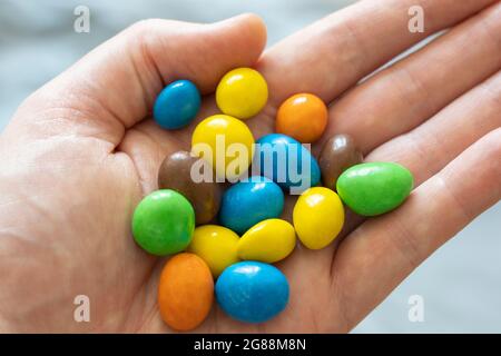 Una mano di un uomo di 40 anni con una selezione di M&M colorati. Tema: Dieta zuccherata, stile di vita malsano, snacking malsano, allergia alle arachidi Foto Stock