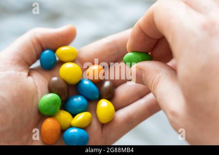 Una mano di un uomo di 40 anni che tiene una selezione di M&M colorati e selezionandone uno. Tema: Dieta zuccherata, stile di vita malsano, snacking malsano Foto Stock