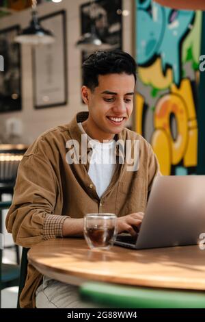 Giovane studente ispanico seduto al tavolo del caffè con computer portatile al coperto Foto Stock