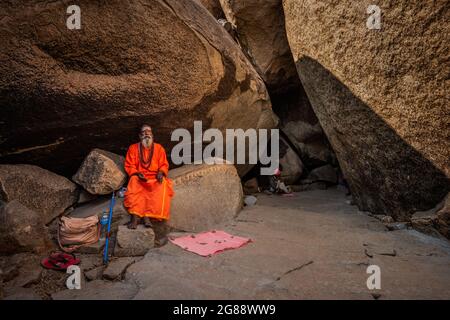 Hampi, Karnataka, India - 11 gennaio 2020 : un monaco vestito d'arancio, seduto tra le pietre del Sentiero di Kampa Bhupa ad Hampi. Foto Stock