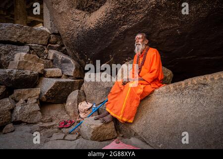 Hampi, Karnataka, India - 11 gennaio 2020 : un monaco vestito d'arancio, seduto tra le pietre del Sentiero di Kampa Bhupa ad Hampi. Foto Stock