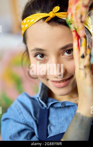 Primo piano ritratto di felice giovane donna, artista femminile guardando la macchina fotografica, posa con le mani in vernice durante la creazione di pittura Foto Stock