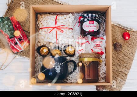 Lviv, Ucraina - 1 dicembre 2017: Marmellata fatta in casa, marshmallow, tazza, raffaello, caramella ferrero, miele in confezione regalo con luci festive. Elegante confezione regalo di dolci Foto Stock