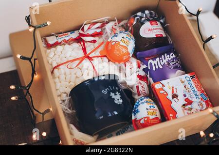 Lviv, Ucraina - 1 dicembre 2017: Marmellata fatta in casa, marshmallow, coppa, raffaello, cioccolatini kinder in scatola regalo con luci natalizie. Elegante confezione regalo di dolci Foto Stock