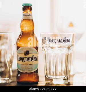Lviv, Ucraina - 1 dicembre 2017: Bottiglia di birra Hoegaarden e bicchiere in calda luce solare sul piano di lavoro in camera. Bevanda deliziosa. Birra Hoegaarden e gla Foto Stock