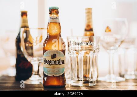 Lviv, Ucraina - 1 dicembre 2017: Bottiglia e bicchiere di birra Hoegaarden in calda luce solare sullo sfondo delle birre Guinness e Leffe sul banco. Hoegaa Foto Stock