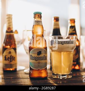 Lviv, Ucraina - 1 dicembre 2017: Bottiglia e bicchiere di birra Hoegaarden con schiuma in luce solare sullo sfondo delle birre Leffe e Grimbergen sul banco. Foto Stock