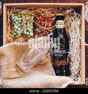 Lviv, Ucraina - 1° dicembre 2017: Bottiglia di birra Guinness e bicchiere con etichetta e spuntini di noci salate sulla paglia in confezione regalo. Elegante confezione regalo per uomo Foto Stock