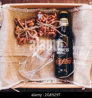 Lviv, Ucraina - 1° dicembre 2017: Bottiglia di birra Guinness, bicchiere e spuntini di noci salate su perlap in confezione regalo. Elegante confezione regalo per compleanno uomo, grasso Foto Stock