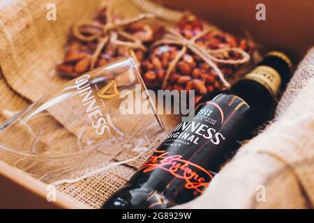 Lviv, Ucraina - 1° dicembre 2017: Bottiglia di birra Guinness, bicchiere e spuntini di noci salate su perlap in confezione regalo. Elegante confezione regalo per compleanno uomo, grasso Foto Stock