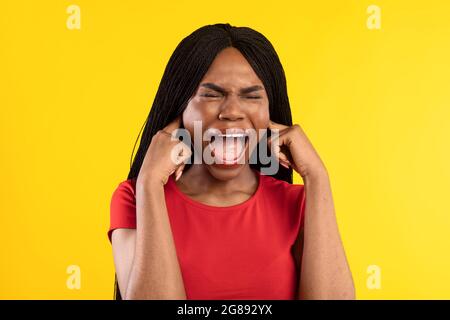 African American Woman gridando orecchie tappanti con le dita, sfondo giallo Foto Stock