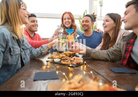 Amici multirazziali che bevono cocktail colorati al bar del ristorante - concetto di amicizia con i giovani che si divertono insieme a tostare bevande su ha Foto Stock