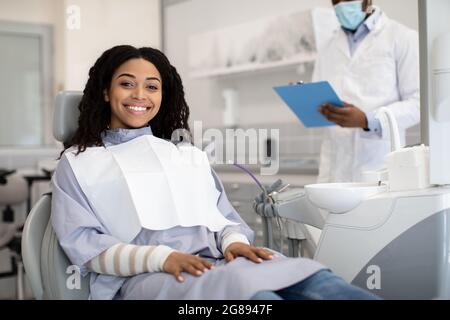 Felice giovane donna africana seduta in sedia durante l'appuntamento in Clinica Stomatologica Foto Stock