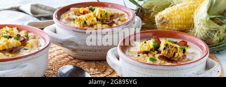 Vista stretta di tre ciotole di pollo e zuppa di mais con mais alla griglia e pancetta, pronti per mangiare. Foto Stock