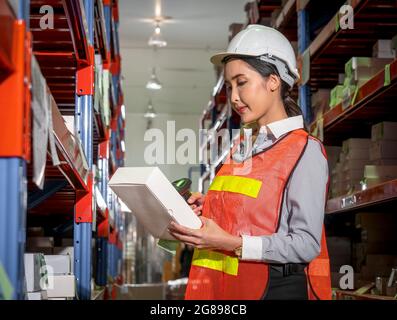 Ritratto di un'operatrice di magazzino sicura in uniforme che tiene uno scanner di prodotto all'interno dell'ambiente di lavoro all'interno del magazzino. Foto Stock