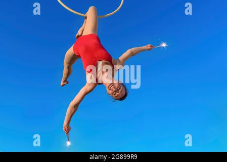 acrobat atletico, giovane gymnast aggraziato che esegue l'esercitazione aerea nell'anello dell'aria all'aperto isolato sullo sfondo che tiene la fontana sparklers. donna Foto Stock