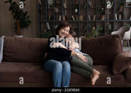 Felice nonna abbracciando e coccolando bella nipote sul divano Foto Stock