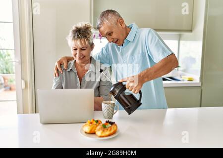Coppia caucasica senior che ha fatto colazione utilizzando un computer portatile in cucina. Foto Stock
