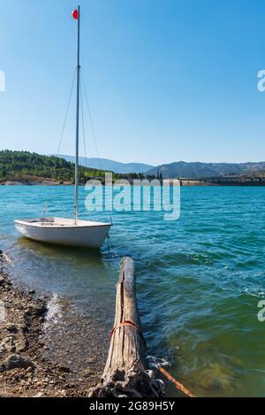 Piccola barca a vela ormeggiata sulla riva ad un ceppo di legno. Foto Stock