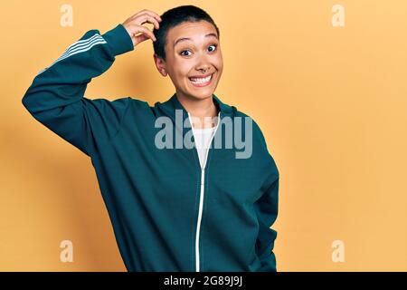 Bella donna ispanica con i capelli corti indossando giacca sportiva confondono e meraviglia circa domanda. Incerta con dubbio, pensando con la mano sulla testa. pe Foto Stock