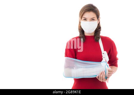 Bella donna asiatica con braccio rotto e bendaggio indossando maschera chirurgica di igiene protettiva in piedi isolato su sfondo bianco con faccia sorridente. INS Foto Stock