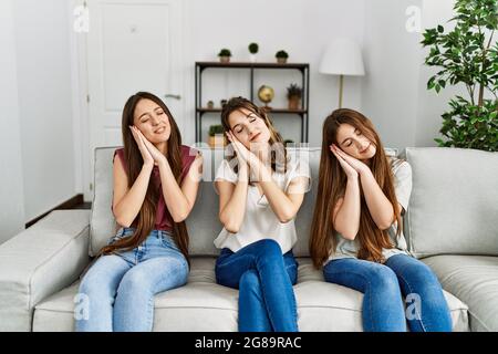 Gruppo di tre ragazze ispaniche sedute sul divano a casa dormendo stanchi sognando e posando con le mani insieme mentre sorride con gli occhi chiusi. Foto Stock