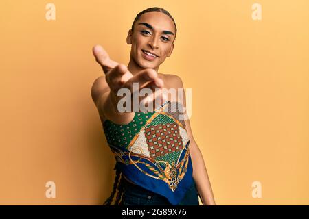 Uomo ispanico che indossa make up e capelli lunghi indossando donna top sorridente amichevole offrendo handshake come saluto e accogliente. Successo di affari. Foto Stock