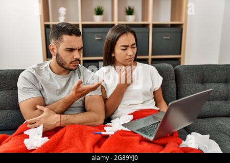 Giovane coppia malata latina che ha teleconsulto medico usando il laptop a casa. Foto Stock