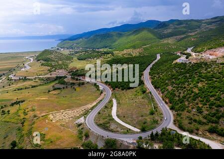 Vista dall'alto sul lago Ohrid, villaggio di pescatori Lin e tortuosa strada panoramica di montagna, preso dal drone. Albania, Europa Foto Stock