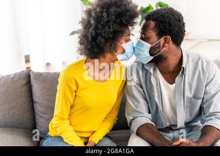 Bella coppia afro-americana a casa coccolare e indossare maschera protettiva viso durante la quarantena covid-19 pandemia Foto Stock