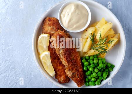 Pesce fritto con piselli verdi, limone e patate fritte Foto Stock