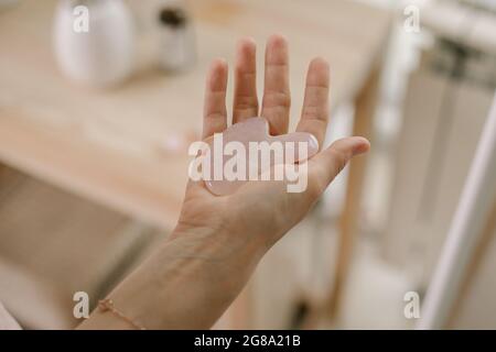 Femmina che tiene il raschietto rosa del gouache per il massaggio del viso mentre fa la procedura di mattina di bellezza in bagno Foto Stock